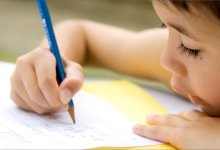 A young student is seen very close up writing on a sheet of paper with a pencil.