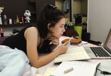 A student studying on her bed with a laptop, textbooks, and notebooks
